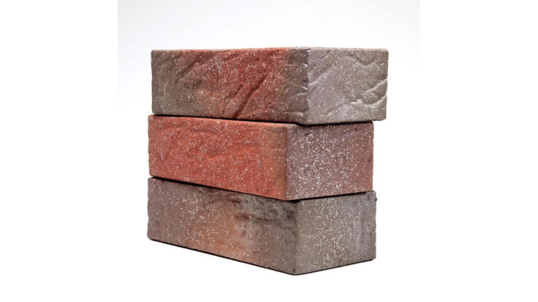 Drei übereinander gestapelte Fassadenziegel in verschiedenen Brauntönen, mit weißen Flecken bedeckt und einer unebenen, leicht strukturierten Oberfläche.